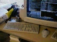 A grainy screencap of a desk with multiple keyboards, and a large CRT monitor with dozens of terminal windows open